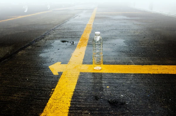 Bottle on yellow line in the rain and fog — Stock Photo, Image