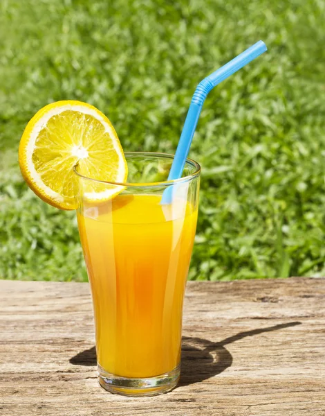 Стакан апельсинового сока на солнце на деревянном столе — стоковое фото