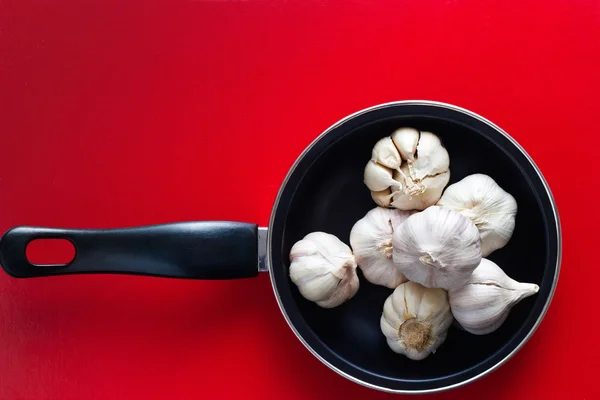 Garlics na panela no fundo vermelho — Fotografia de Stock