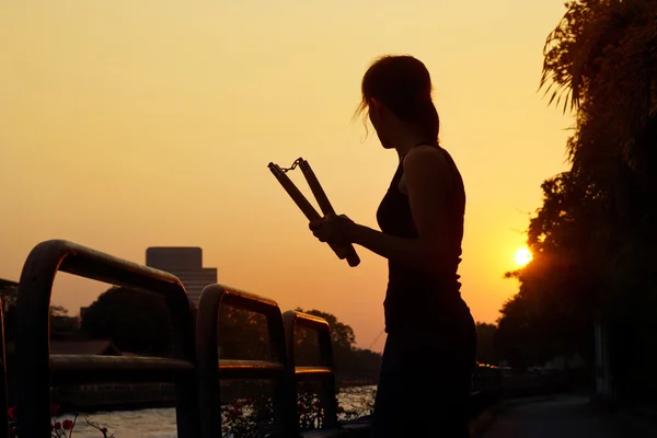 Mujer con nunchaku en las manos silueta en la puesta del sol, artes marciales — Foto de Stock