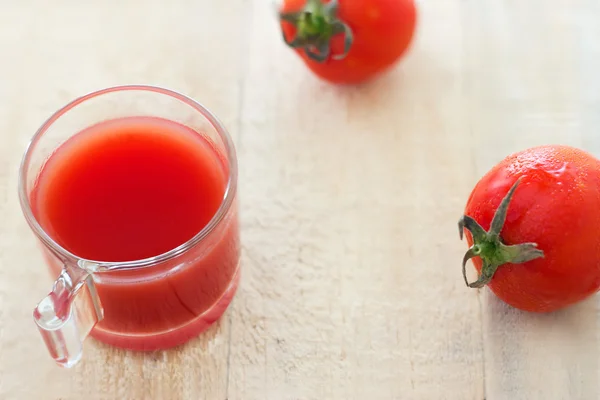 Fresh tomato juice in the grass and a few of tomato on pale wooden background