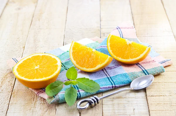 Orangensegmentscheiben mit Minze und Edelstahllöffel auf pastellfarbenem Stoff und hölzernem Hintergrund — Stockfoto