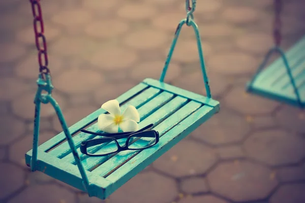 vintage color tone style, glasses and white flower on the blue swing