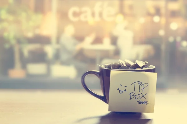 Tip box, monete nella tazza di caffè davanti allo specchio, colore vintage e soft focus — Foto Stock