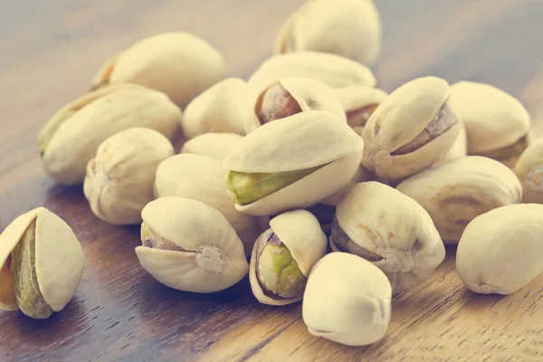 Heap salted pistachio nuts on wooden background, vintage color tone — Stock Photo, Image