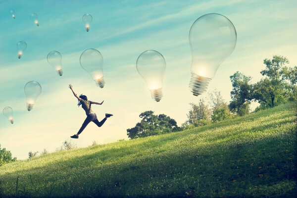 Абстрактная женщина бегает и прыгает за лампочкой на зеленой траве и цветочном поле
