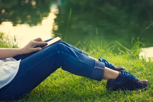Nő segítségével mobil okos telefon, a lába, zöld a fű és a tó háttér — Stock Fotó