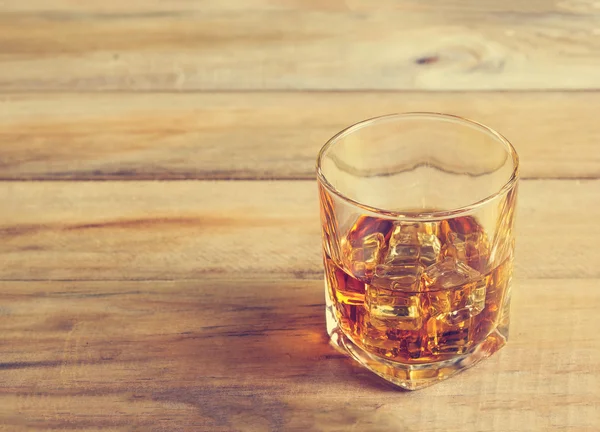 Vaso de whisky con hielo sobre fondo de madera, tono de color vintage — Foto de Stock