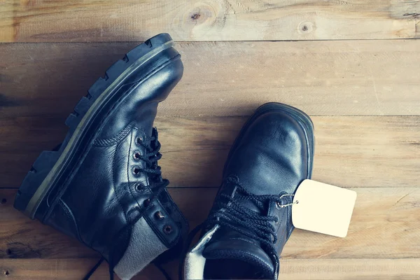 Černé boty s popiskem tag na dřevěné pozadí, vintage barevný tón — Stock fotografie