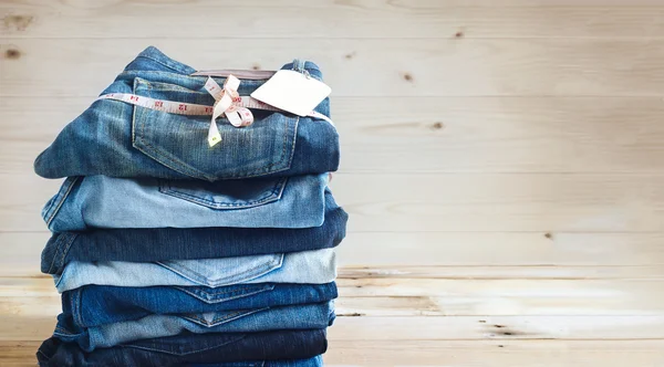 Jeans com medida e etiqueta empilhados em um fundo de madeira — Fotografia de Stock