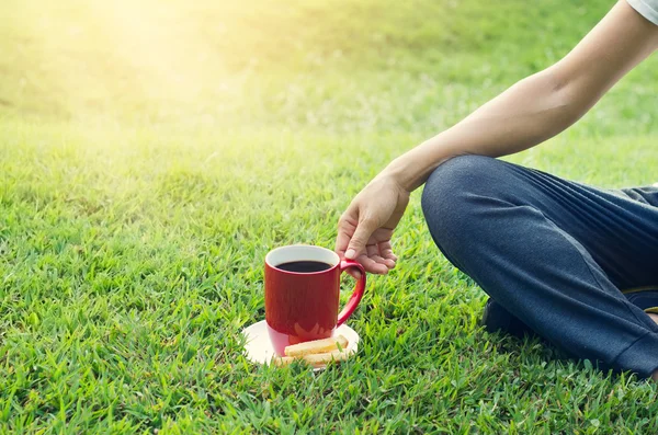 Mulher com copo de café vermelho relaxante no fundo da grama — Fotografia de Stock