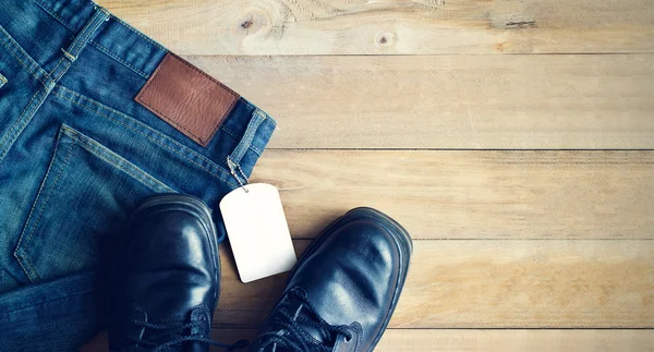 Pantalones vaqueros azules con etiqueta blanca en blanco y zapatos sobre fondo de madera —  Fotos de Stock