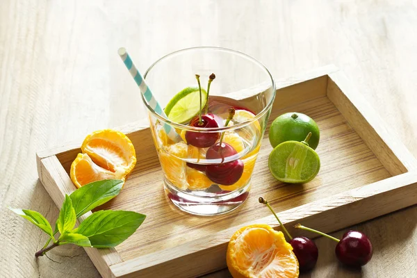 Egészséges méregtelenítés víz, cseresznye, a narancs és a lime, a fa tálcán pohár — Stock Fotó