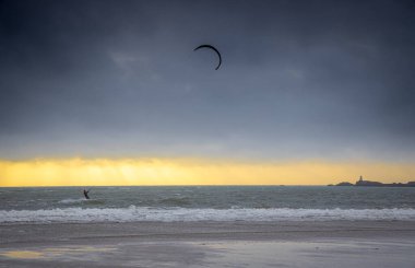 Bir uçurtma sörfçüsü, İngiltere 'nin deniz kıyısında, büyük bir kontrol edilebilir güç uçurtmasıyla rüzgarın gücünü kontrol ediyor.