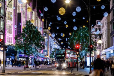 Londra 'nın kırmızı otobüsü Noel süslemeleri ve yoğun yaya trafiğiyle aydınlık bir caddeden geçiyor. Seyahat, tatil veya kentsel yaşam tarzı temaları için ideal