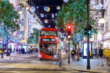 Londra 'nın kırmızı otobüsü Noel süslemeleri ve yoğun yaya trafiğiyle aydınlık bir caddeden geçiyor. Seyahat, tatil veya kentsel yaşam tarzı temaları için ideal