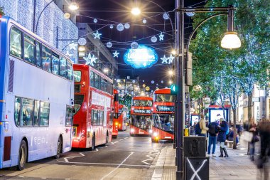 Londra 'nın kırmızı otobüsü Noel süslemeleri ve yoğun yaya trafiğiyle aydınlık bir caddeden geçiyor. Seyahat, tatil veya kentsel yaşam tarzı temaları için ideal