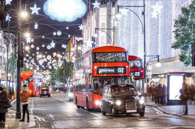 Londra 'nın kırmızı otobüsü Noel süslemeleri ve yoğun yaya trafiğiyle aydınlık bir caddeden geçiyor. Seyahat, tatil veya kentsel yaşam tarzı temaları için ideal