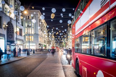 Londra 'nın kırmızı otobüsü Noel süslemeleri ve yoğun yaya trafiğiyle aydınlık bir caddeden geçiyor. Seyahat, tatil veya kentsel yaşam tarzı temaları için ideal