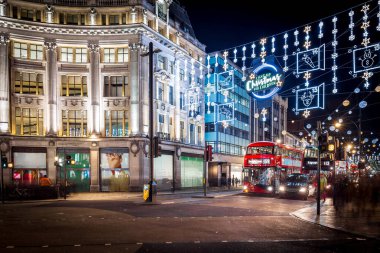 Londra 'nın kırmızı otobüsü Noel süslemeleri ve yoğun yaya trafiğiyle aydınlık bir caddeden geçiyor. Seyahat, tatil veya kentsel yaşam tarzı temaları için ideal