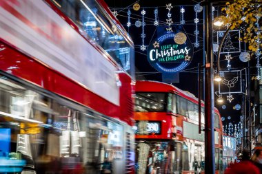 Londra 'nın kırmızı otobüsü Noel süslemeleri ve yoğun yaya trafiğiyle aydınlık bir caddeden geçiyor. Seyahat, tatil veya kentsel yaşam tarzı temaları için ideal