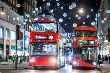 Londra 'nın kırmızı otobüsü Noel süslemeleri ve yoğun yaya trafiğiyle aydınlık bir caddeden geçiyor. Seyahat, tatil veya kentsel yaşam tarzı temaları için ideal