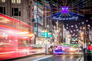 Londra 'nın kırmızı otobüsü Noel süslemeleri ve yoğun yaya trafiğiyle aydınlık bir caddeden geçiyor. Seyahat, tatil veya kentsel yaşam tarzı temaları için ideal