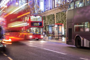 Londra 'nın kırmızı otobüsü Noel süslemeleri ve yoğun yaya trafiğiyle aydınlık bir caddeden geçiyor. Seyahat, tatil veya kentsel yaşam tarzı temaları için ideal