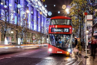 Londra 'nın kırmızı otobüsü Noel süslemeleri ve yoğun yaya trafiğiyle aydınlık bir caddeden geçiyor. Seyahat, tatil veya kentsel yaşam tarzı temaları için ideal