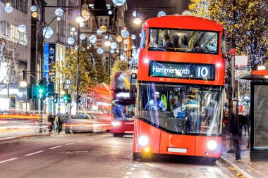 Londra 'nın kırmızı otobüsü Noel süslemeleri ve yoğun yaya trafiğiyle aydınlık bir caddeden geçiyor. Seyahat, tatil veya kentsel yaşam tarzı temaları için ideal
