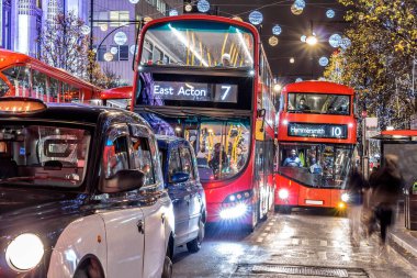 Londra 'nın kırmızı otobüsü Noel süslemeleri ve yoğun yaya trafiğiyle aydınlık bir caddeden geçiyor. Seyahat, tatil veya kentsel yaşam tarzı temaları için ideal
