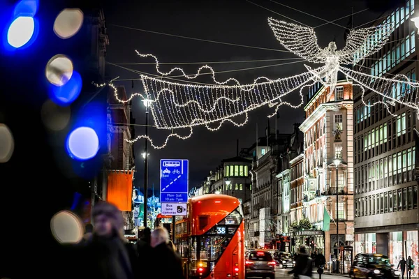 Londra 'nın kırmızı otobüsü Noel süslemeleri ve yoğun yaya trafiğiyle aydınlık bir caddeden geçiyor. Seyahat, tatil veya kentsel yaşam tarzı temaları için ideal