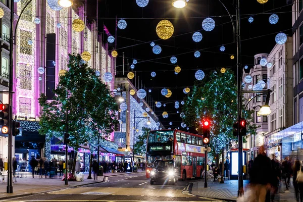 Londra 'nın kırmızı otobüsü Noel süslemeleri ve yoğun yaya trafiğiyle aydınlık bir caddeden geçiyor. Seyahat, tatil veya kentsel yaşam tarzı temaları için ideal