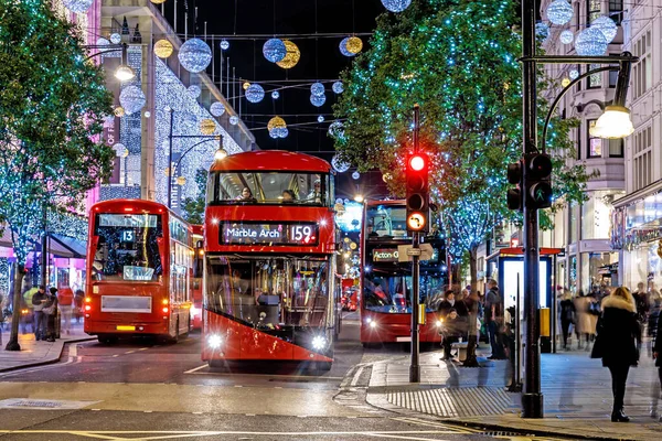 Londra 'nın kırmızı otobüsü Noel süslemeleri ve yoğun yaya trafiğiyle aydınlık bir caddeden geçiyor. Seyahat, tatil veya kentsel yaşam tarzı temaları için ideal