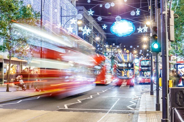 Londra 'nın kırmızı otobüsü Noel süslemeleri ve yoğun yaya trafiğiyle aydınlık bir caddeden geçiyor. Seyahat, tatil veya kentsel yaşam tarzı temaları için ideal