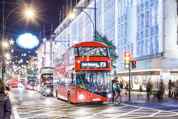 Londra 'nın kırmızı otobüsü Noel süslemeleri ve yoğun yaya trafiğiyle aydınlık bir caddeden geçiyor. Seyahat, tatil veya kentsel yaşam tarzı temaları için ideal