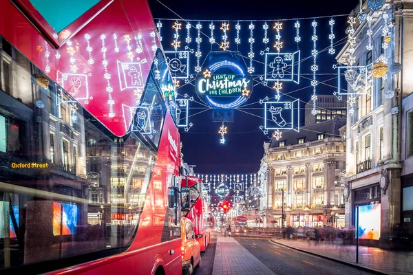 Londra 'nın kırmızı otobüsü Noel süslemeleri ve yoğun yaya trafiğiyle aydınlık bir caddeden geçiyor. Seyahat, tatil veya kentsel yaşam tarzı temaları için ideal