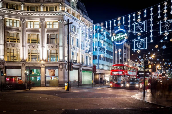 Londra 'nın kırmızı otobüsü Noel süslemeleri ve yoğun yaya trafiğiyle aydınlık bir caddeden geçiyor. Seyahat, tatil veya kentsel yaşam tarzı temaları için ideal