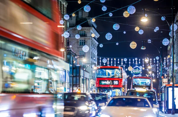 Londra 'nın kırmızı otobüsü Noel süslemeleri ve yoğun yaya trafiğiyle aydınlık bir caddeden geçiyor. Seyahat, tatil veya kentsel yaşam tarzı temaları için ideal