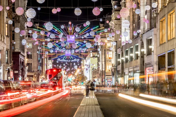 Londra 'nın kırmızı otobüsü Noel süslemeleri ve yoğun yaya trafiğiyle aydınlık bir caddeden geçiyor. Seyahat, tatil veya kentsel yaşam tarzı temaları için ideal