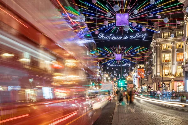 Londra 'nın kırmızı otobüsü Noel süslemeleri ve yoğun yaya trafiğiyle aydınlık bir caddeden geçiyor. Seyahat, tatil veya kentsel yaşam tarzı temaları için ideal
