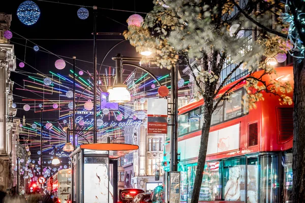 Londra 'nın kırmızı otobüsü Noel süslemeleri ve yoğun yaya trafiğiyle aydınlık bir caddeden geçiyor. Seyahat, tatil veya kentsel yaşam tarzı temaları için ideal