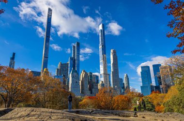 Central Park manzarası, New York 'ta açık mavi gökyüzü altında altın sonbahar ağaçları ve şehir kuleleri ile kaplıdır; seyahat, refah, emlak ve yaşam tarzı markalaşması için mükemmeldir.
