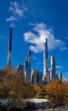 Central Park manzarası, New York 'ta açık mavi gökyüzü altında altın sonbahar ağaçları ve şehir kuleleri ile kaplıdır; seyahat, refah, emlak ve yaşam tarzı markalaşması için mükemmeldir.