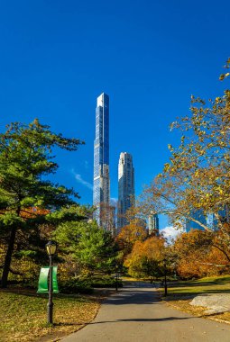 Central Park manzarası, New York 'ta açık mavi gökyüzü altında altın sonbahar ağaçları ve şehir kuleleri ile kaplıdır; seyahat, refah, emlak ve yaşam tarzı markalaşması için mükemmeldir.