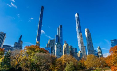 Central Park manzarası, New York 'ta açık mavi gökyüzü altında altın sonbahar ağaçları ve şehir kuleleri ile kaplıdır; seyahat, refah, emlak ve yaşam tarzı markalaşması için mükemmeldir.