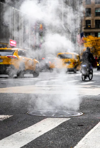 Trafik ve bayraklar hafifçe bulanık, kentsel altyapı, enerji ve kış hava durumu editörleri için ideal New York City Bulvarı 'ndaki rögar kapağından yoğun buhar dalgaları
