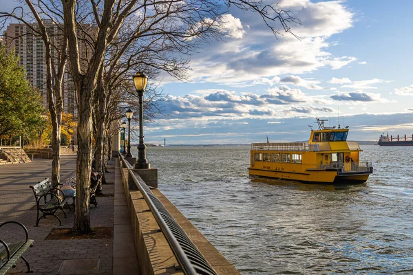 Sarı yolcu feribotu, Manhattan 'daki Battery Park' ın yanındaki Hudson 'da dramatik bulutlar altında seyahat eder; seyahat reklamları, New York turizmi, ulaşım ve şehir yaşam tarzı temaları için ideal
