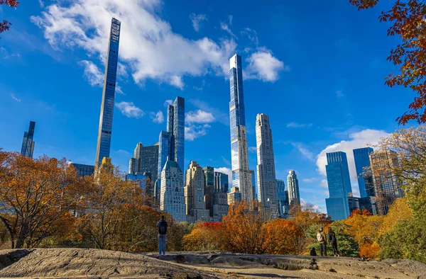 Central Park manzarası, New York 'ta açık mavi gökyüzü altında altın sonbahar ağaçları ve şehir kuleleri ile kaplıdır; seyahat, refah, emlak ve yaşam tarzı markalaşması için mükemmeldir.
