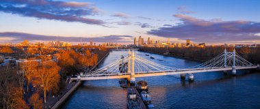 Londra 'nın ufuk çizgisi parlarken Chelsea ve Battersea' yi birbirine bağlayan Thames Nehri üzerindeki Albert Köprüsü 'nün panoramik görüntüsü seyahat, ulaşım, gayrimenkul ve şehir markası